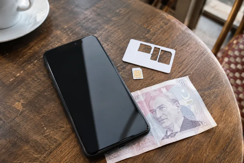 Смартфон, SIM-карта и лоток для неё на столе рядом с турецкими лирами