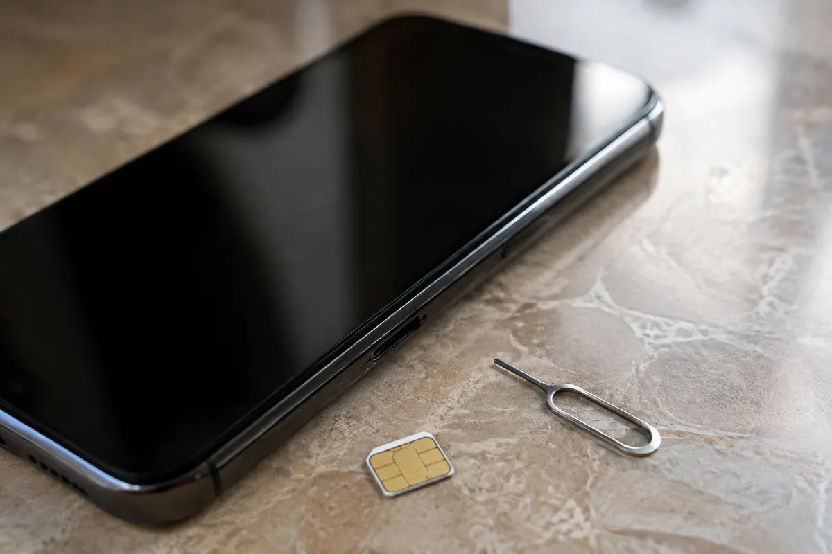 Смартфон, SIM-карта и извлечённый лоток для SIM-карты на деревянном столе